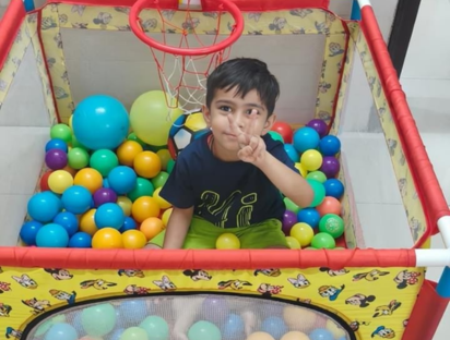 Boy playing inside a colourful ball pit with a basketball hoop