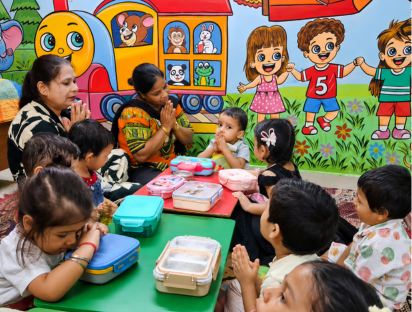 Children and teachers seated together around the lunch table in the classroom