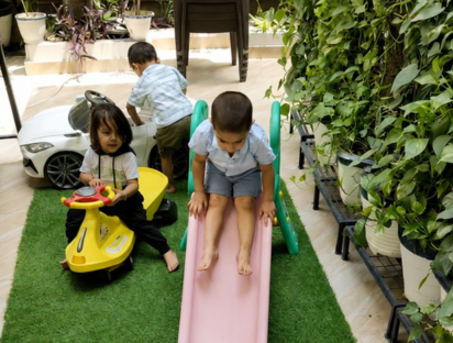 Children playing on a pink slide and a yellow ride-on car in the green play area