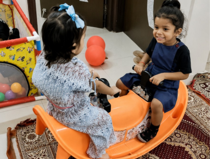 Two children smiling while playing on an orange seesaw ride indoors