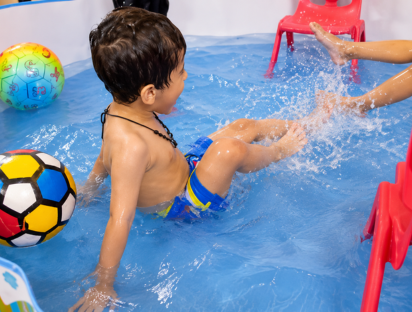 Child splashing happily in the pool with colourful balls during the pool party
